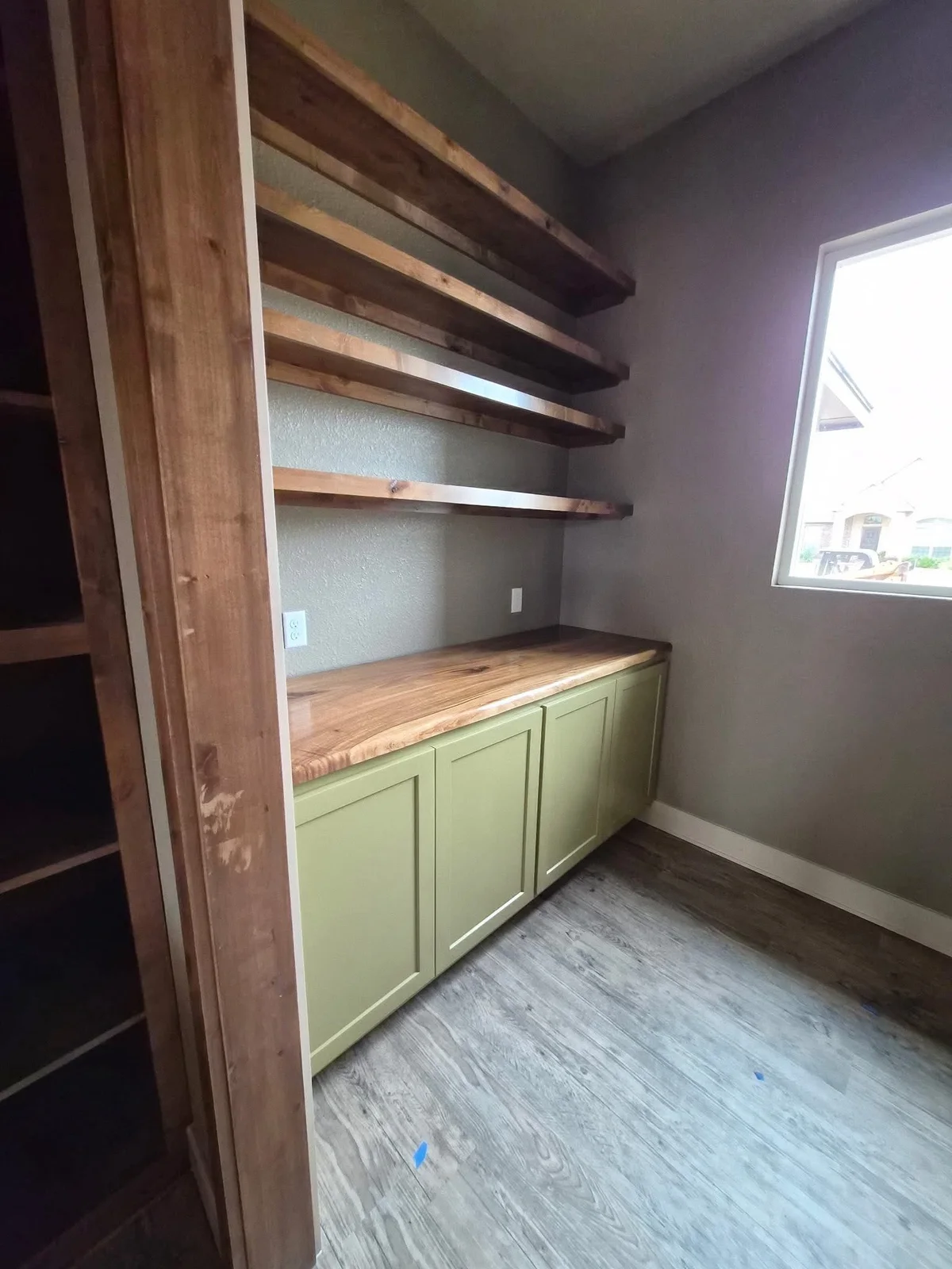 Green lower cabinets beneath a wood counter and open wooden shelves