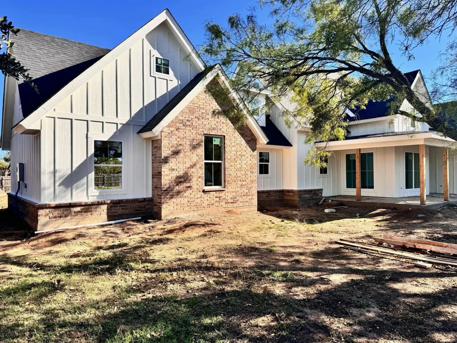 White siding and brickwork on a house exterior beneath a tree