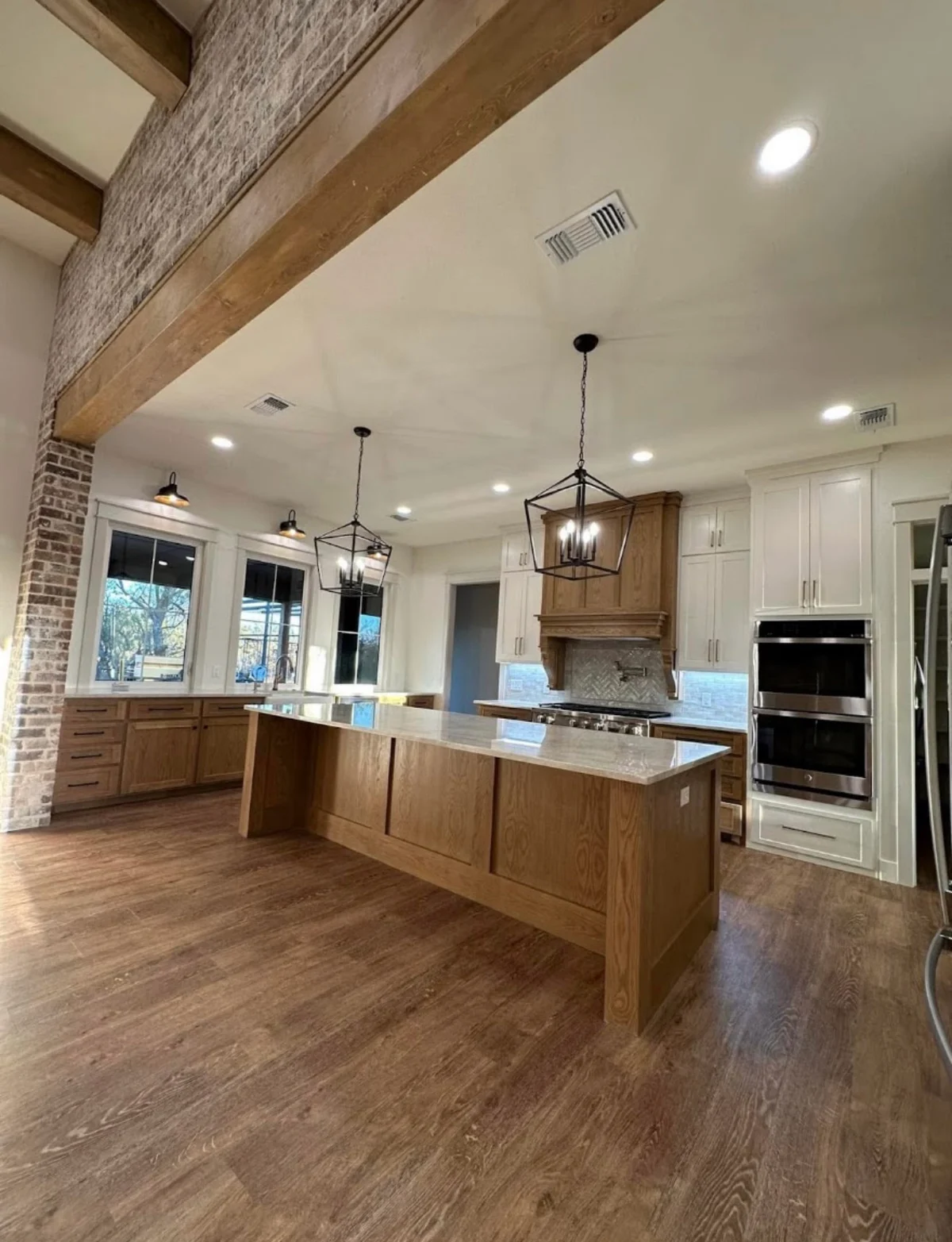 White upper cabinets and wood cabinetry beneath exposed beams and lantern pendant lights